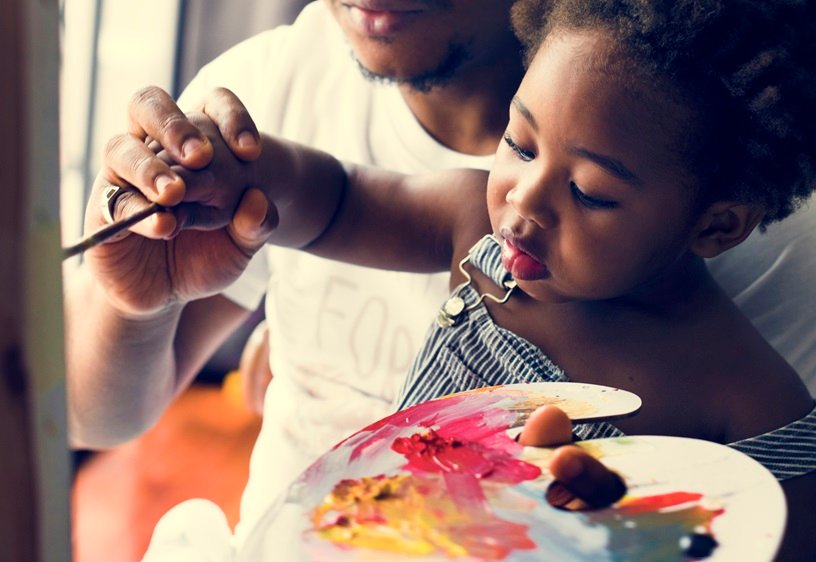 African descent dad teaching his child how to paint